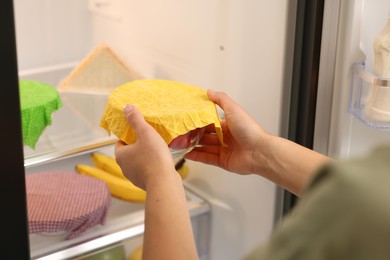 Photo of Woman putting bowl covered with beeswax food wrap into refrigerator, closeup