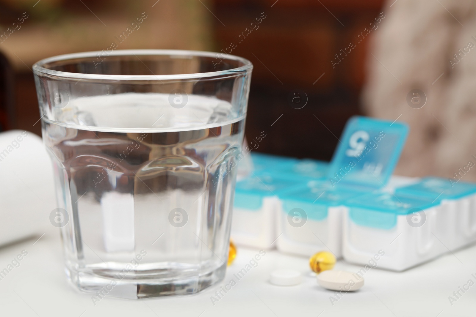 Photo of Plastic pill box with different medicaments indoors, focus on glass of water. Space for text