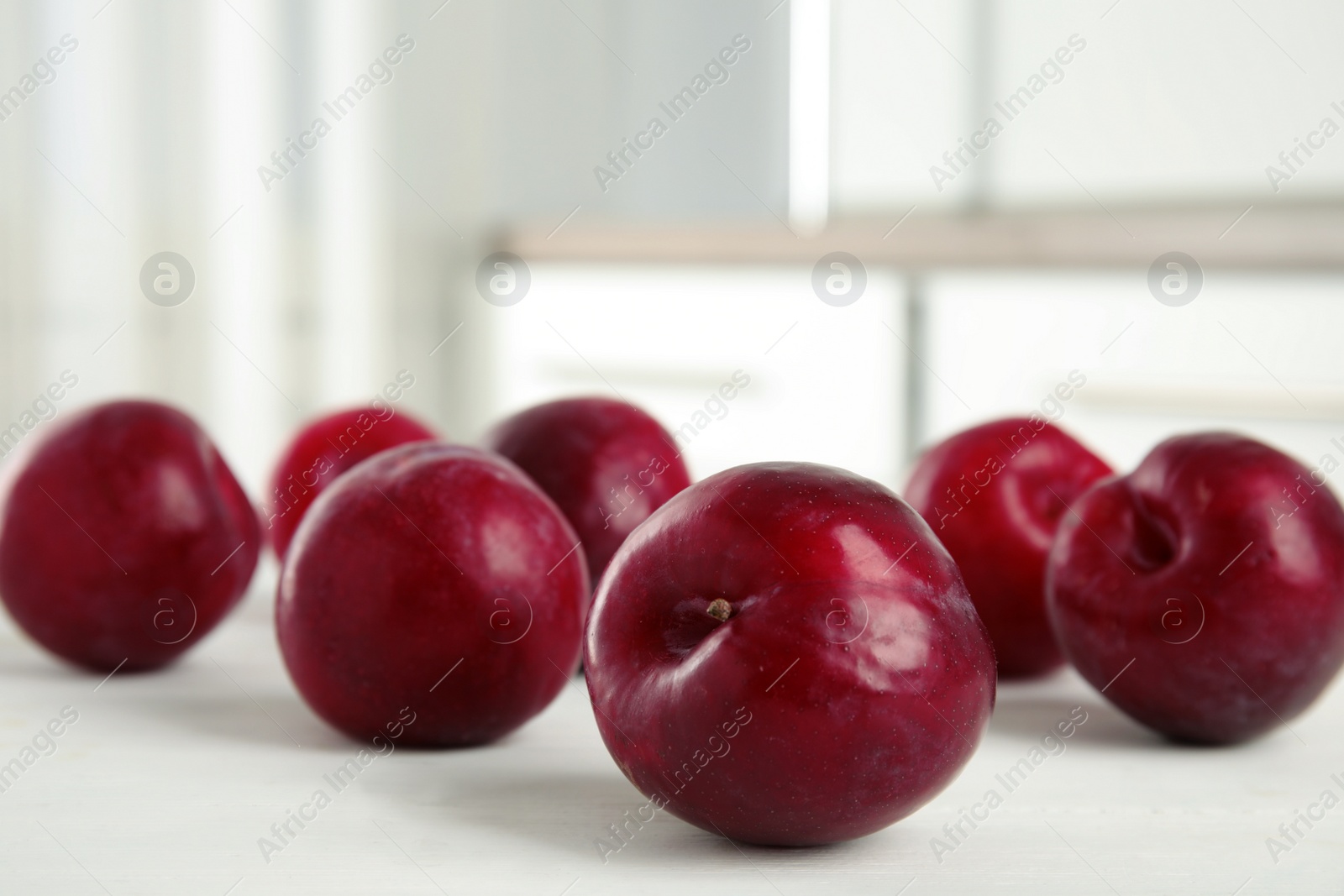 Photo of Delicious ripe plums on white wooden table, closeup. Space for text