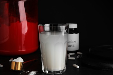 Photo of Amino acid shake, powder, pills and weight plates on black background