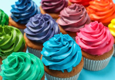 Many delicious colorful cupcakes on light blue background, closeup