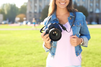 Photo of Young female photographer holding professional camera on street. Space for text