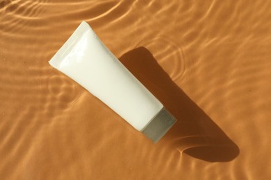 Tube with moisturizing cream in water on orange background, top view