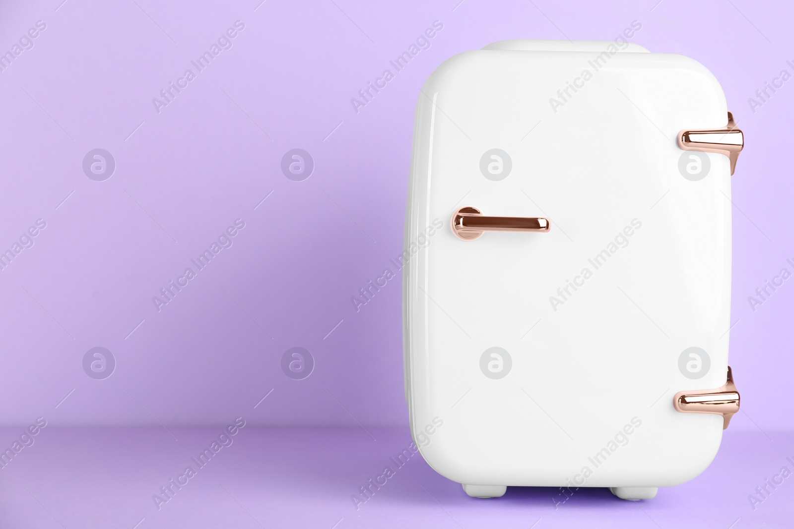 Photo of Cosmetic refrigerator on violet background, space for text