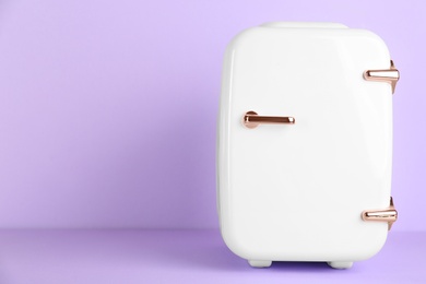 Cosmetic refrigerator on violet background, space for text