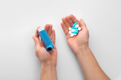 Photo of Man holding asthma inhaler and pills on white background, top view