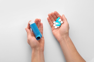 Man holding asthma inhaler and pills on white background, top view