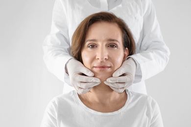 Photo of Doctor examining mature woman face before cosmetic surgery on white background