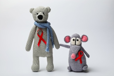 Photo of Cute knitted toys with red ribbons on light grey background. AIDS disease awareness