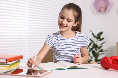Photo of E-learning. Cute girl using tablet for studying online at table indoors