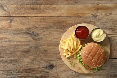 Photo of Delicious burger with beef patty, sauce and french fries on wooden table, top view. Space for text