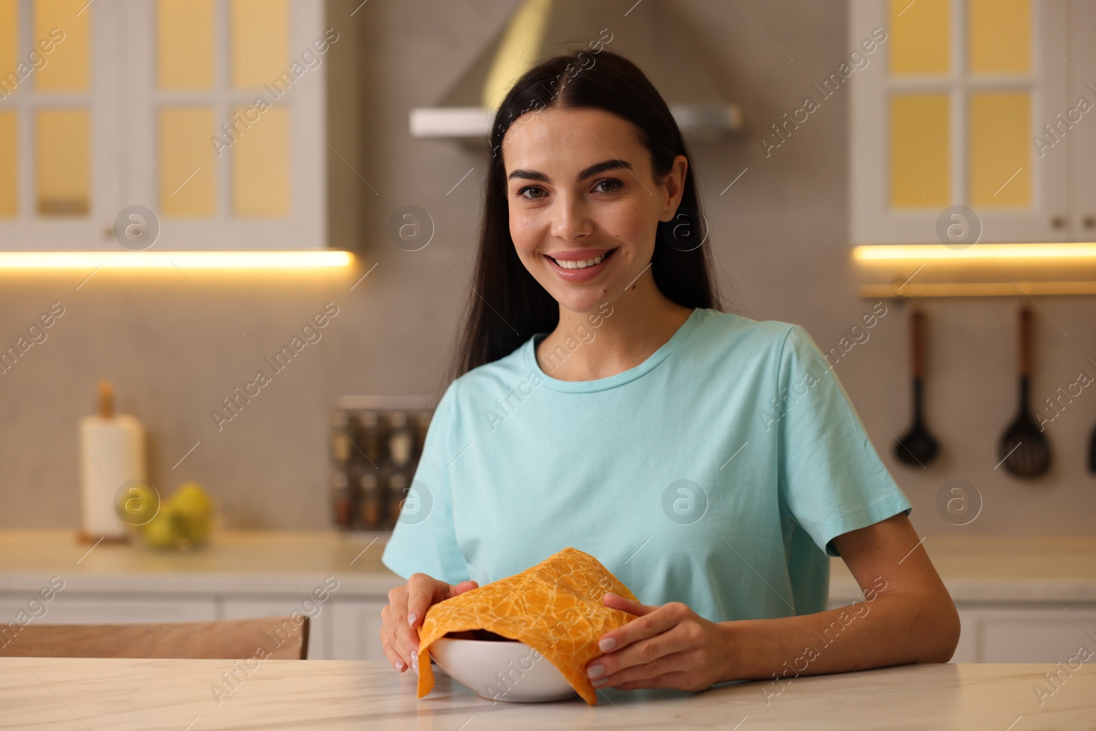 Photo of Happy woman packing bowl into beeswax food wrap at table in kitchen