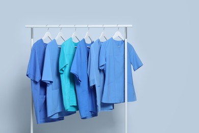 Photo of Different medical uniforms on rack against light grey background. Space for text