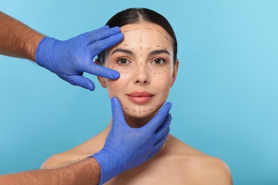 Photo of Doctor checking patient's face before cosmetic surgery operation on light blue background