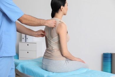 Photo of Orthopedist helping patient to put on posture corrector in clinic, closeup. Scoliosis treatment