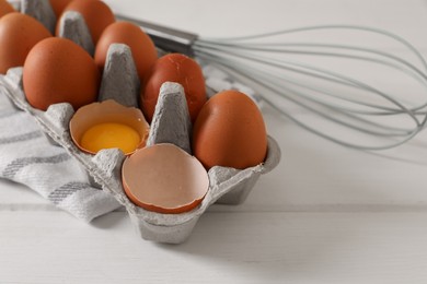 Photo of Fresh raw chicken eggs and whisk on white wooden table, closeup. Space for text