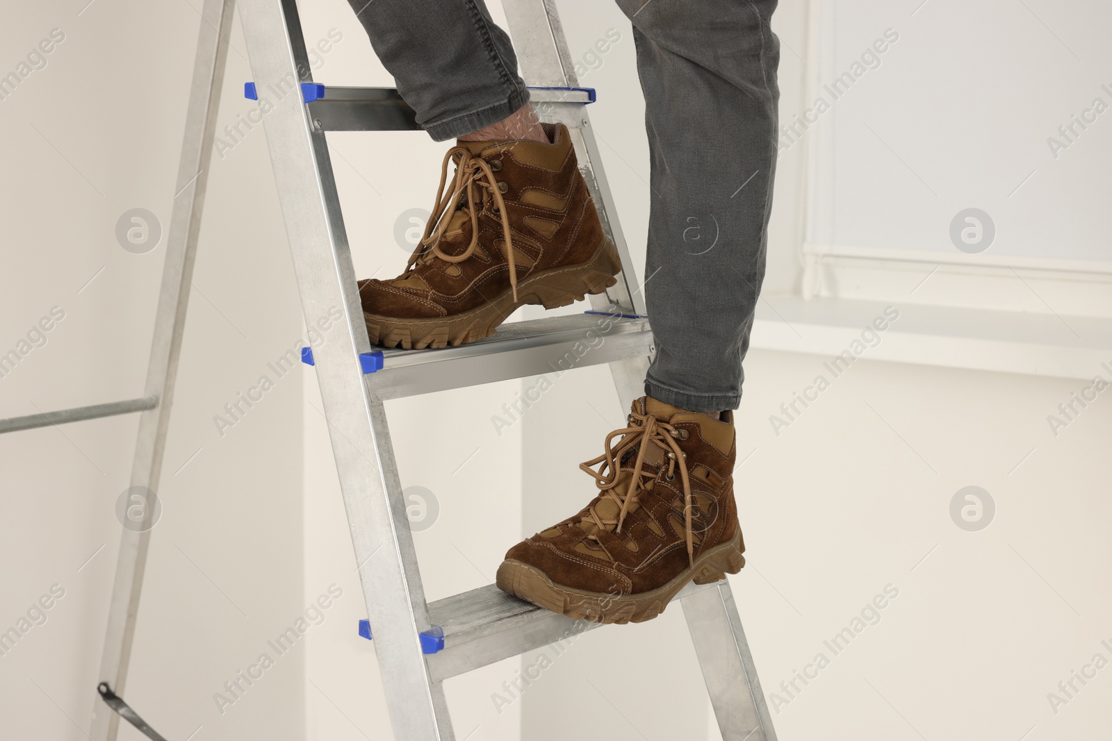 Photo of Man climbing up metal stepladder near white wall indoors closeup. Room renovation