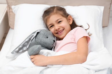 Photo of Cute child with stuffed rabbit resting in bed at hospital