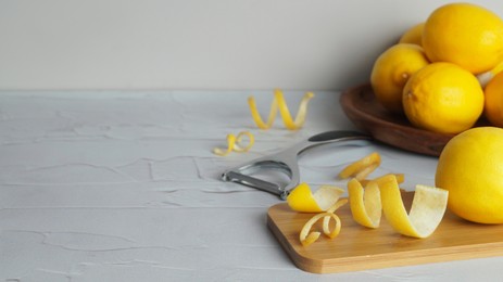 Photo of Wooden board, lemons, peeler and fresh rind on white textured table. Space for text
