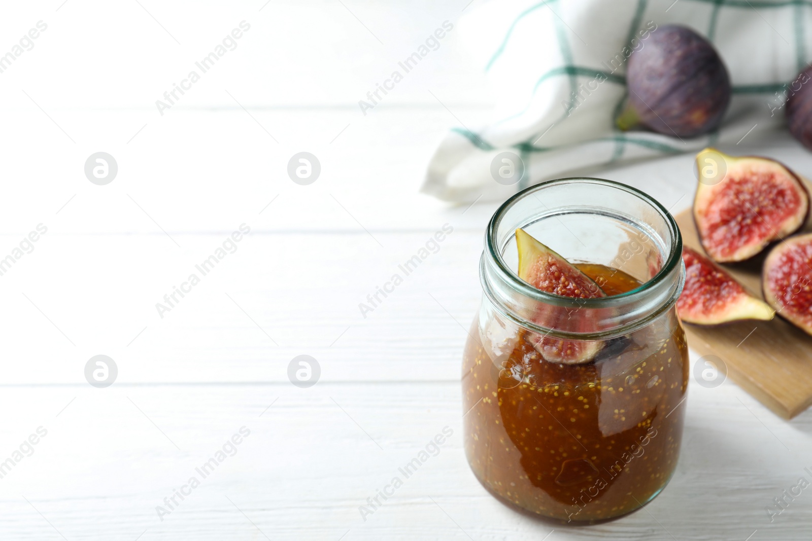 Photo of Delicious fig jam on white wooden table. Space for text