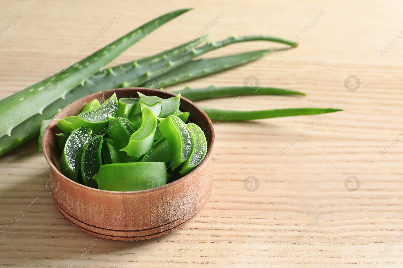 Photo of Bowl with sliced aloe vera leaves and space for text on wooden table