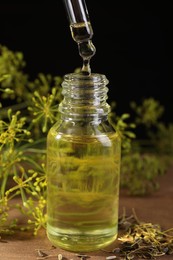 Photo of Dripping dill essential oil from pipette into bottle on wooden table, closeup