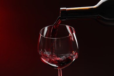 Photo of Pouring red wine from bottle into glass on dark background, closeup