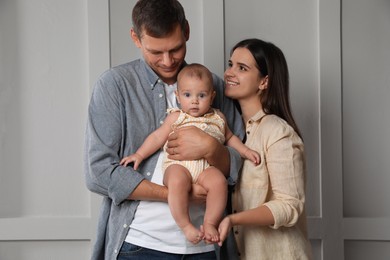 Photo of Happy family. Couple with their cute baby near light wall