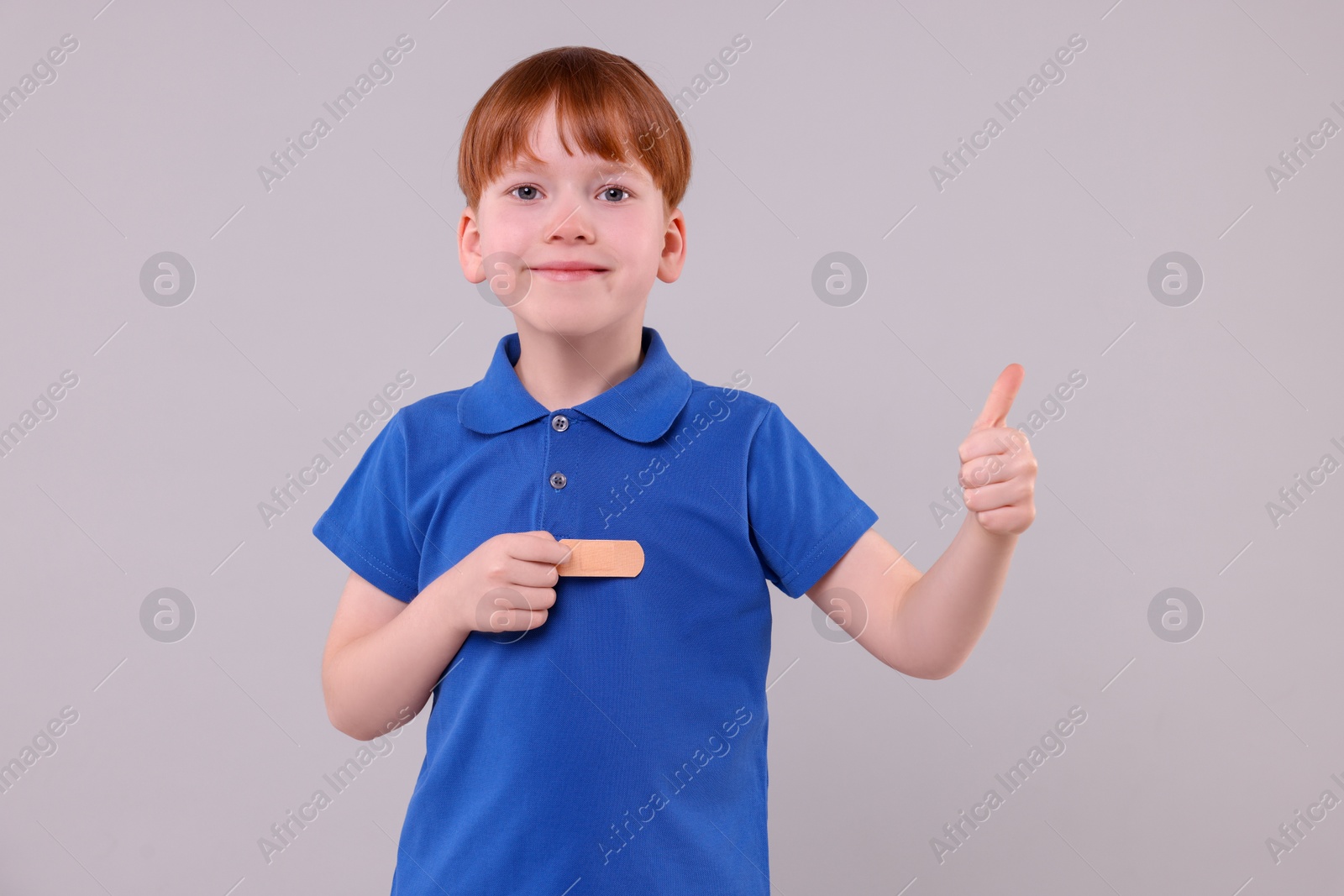 Photo of Little boy with sticking tape showing thumb up on light grey background