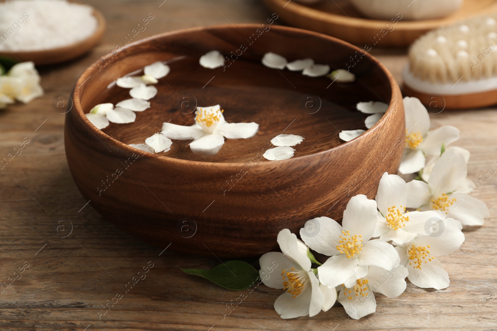 Photo of Bowl with water and beautiful jasmine flowers on wooden table