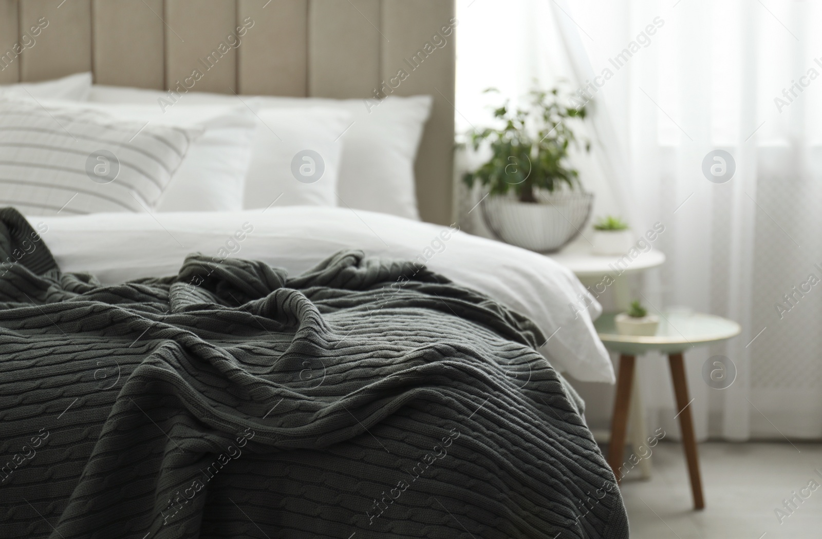 Photo of Comfortable bed with warm knitted plaid indoors