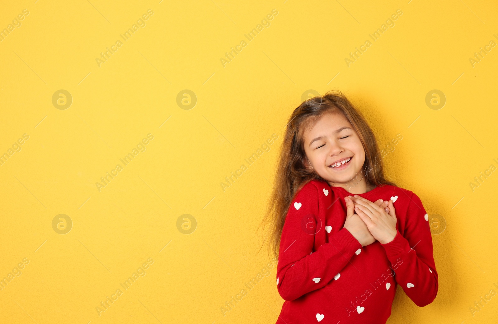 Photo of Portrait of girl holding hands near her heart on color background. Space for text