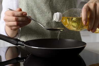 Photo of Woman with spoon pouring cooking oil into frying pan on stove, closeup