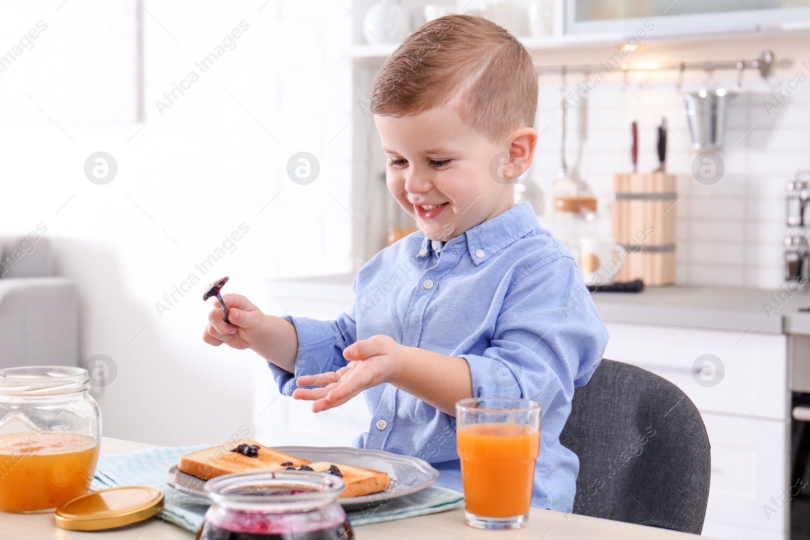 Photo of Cute little boy spreading sweet jam onto toast at table