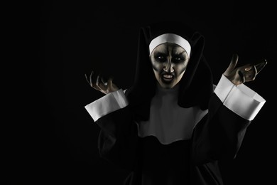 Photo of Portrait of scary devilish nun on black background, space for text. Halloween party look