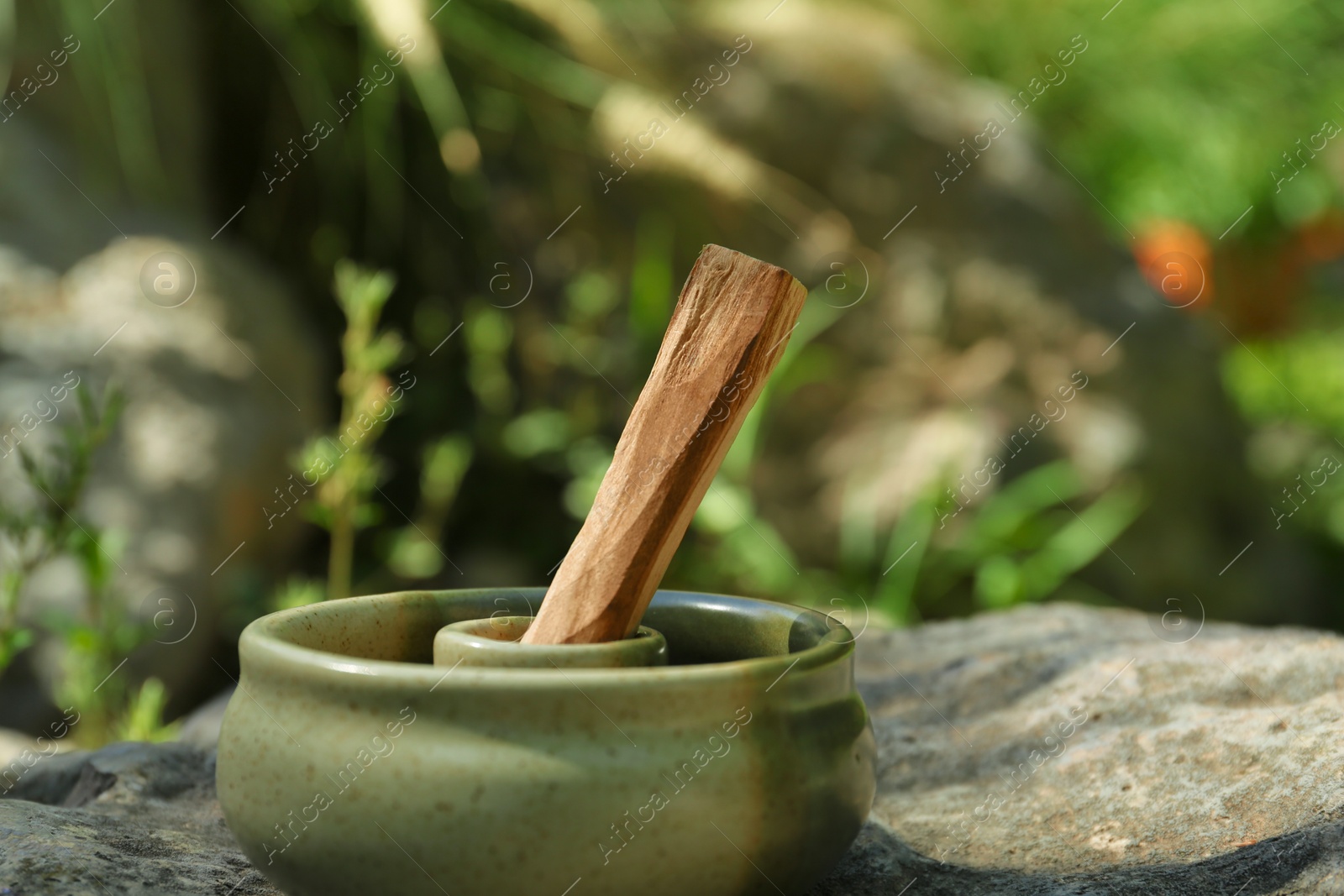 Photo of Palo santo stick in holder on stone outdoors, closeup