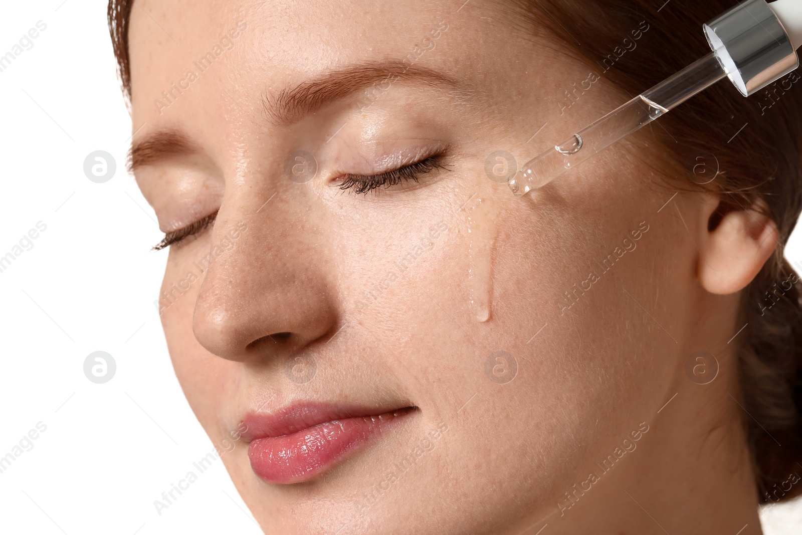 Photo of Beautiful woman with freckles applying cosmetic serum onto her face on white background, closeup