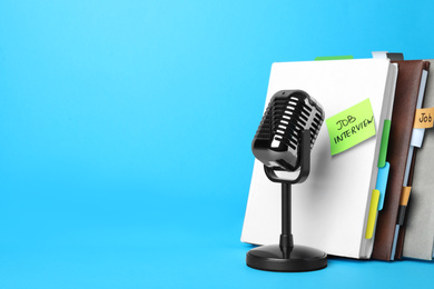 Photo of Retro microphone, notebooks and reminder note with words JOB INTERVIEW on light blue background, space for text