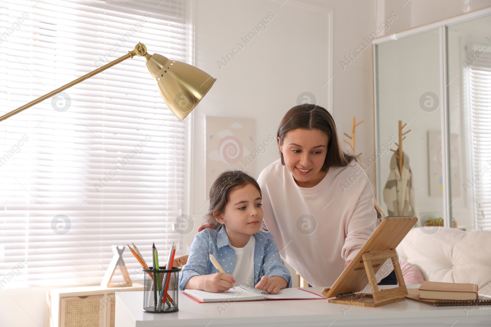 Photo of Mother helping her daughter with homework using tablet at home