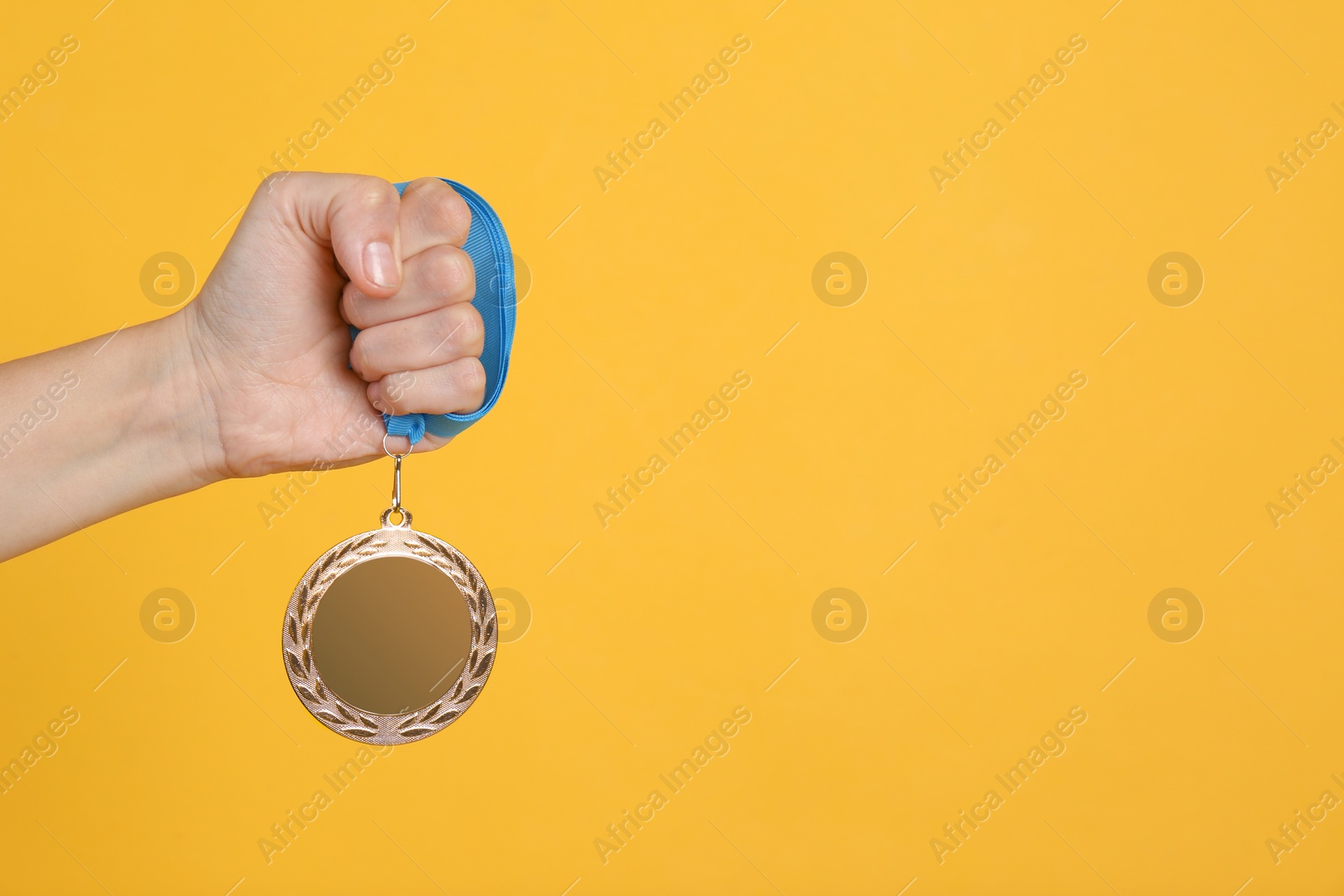 Photo of Woman holding bronze medal on yellow background, closeup. Space for design