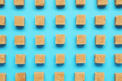 Photo of Brown sugar cubes on turquoise background, flat lay