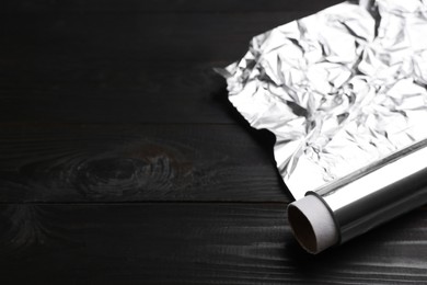 Photo of Roll of aluminum foil on dark wooden table, closeup. Space for text