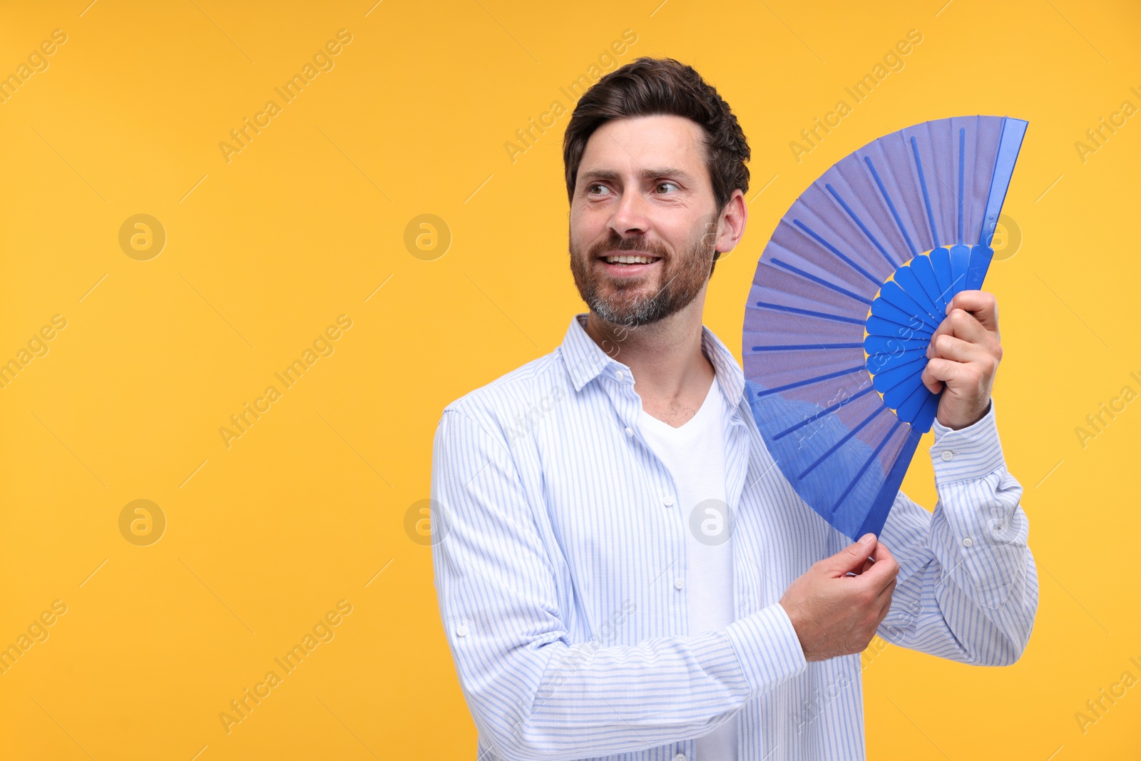 Photo of Happy man holding hand fan on orange background. Space for text