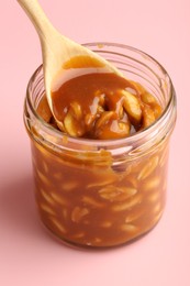 Taking tasty salted caramel with peanuts from jar on pink background, closeup