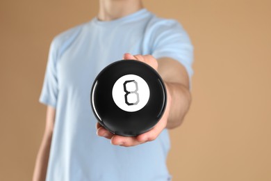 Photo of Man holding magic eight ball on light brown background, closeup. Space for text