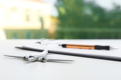 Photo of Toy plane and clipboard with documents on white table. Travel insurance