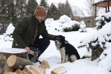 Photo of Man with axe and wood petting cute dog outdoors