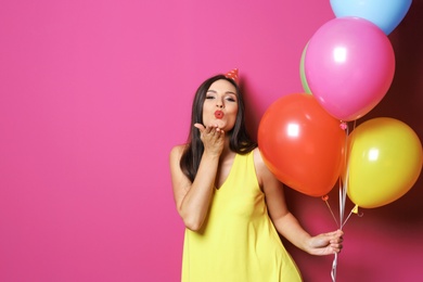 Young woman with bright balloons on color background. Birthday celebration