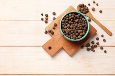 Photo of Dry allspice berries (Jamaica pepper) in bowl and spoon on light wooden table, flat lay. Space for text