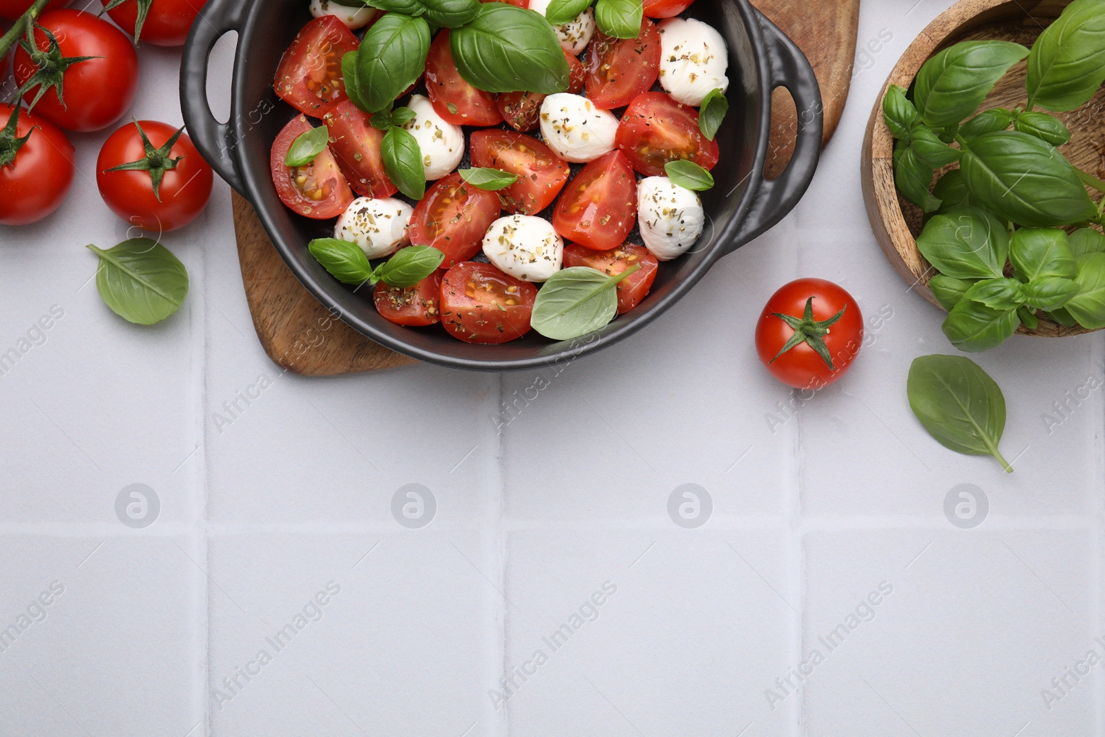 Photo of Tasty salad Caprese with mozarella balls, tomatoes and basil on white tiled table, flat lay. Space for text